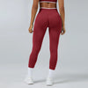 A model wearing maroon high-waist yoga leggings and a matching sports bra, standing in a studio setting.
