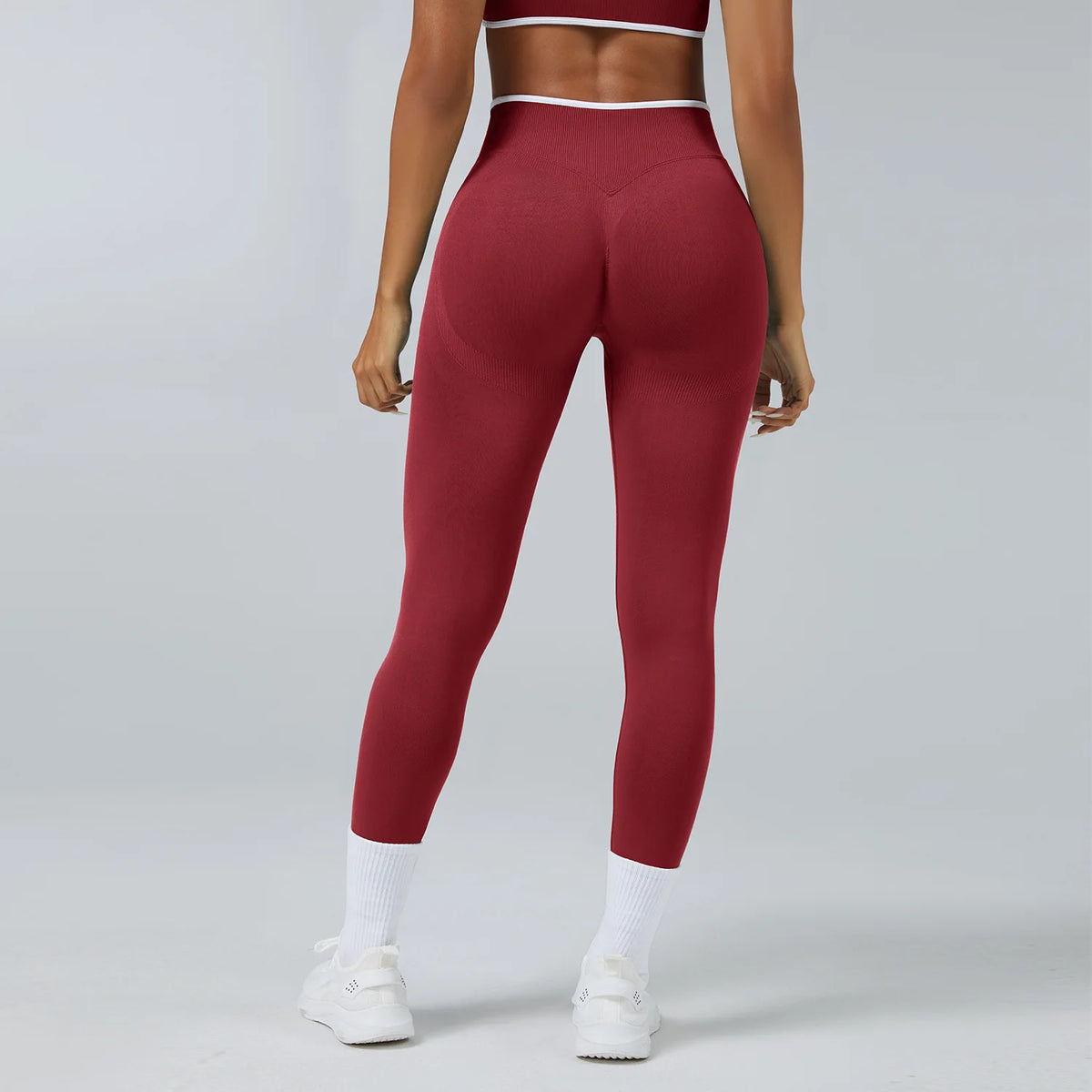 A model wearing maroon high-waist yoga leggings and a matching sports bra, standing in a studio setting.