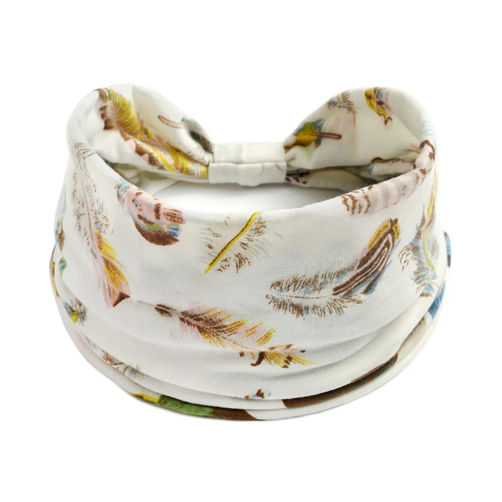 A white cotton stretch headband with a floral pattern featuring dried grasses and feathers.