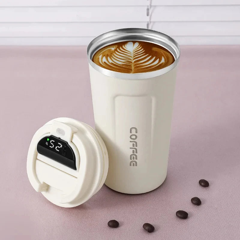 A white insulated thermos bottle with a lid and a coffee latte inside, resting on a pink surface.
