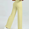 A woman is modeling light yellow high waisted yoga pants while standing.