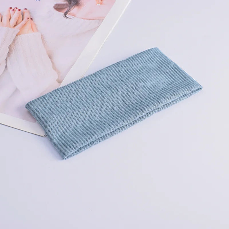 A light blue knitted headband is shown resting on a white surface next to a piece of paper.