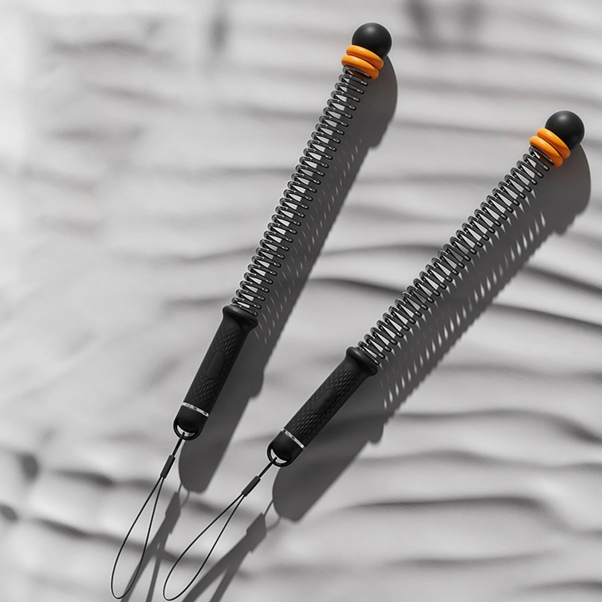 A close-up of adjustable ropeless battle ropes with black handles and orange accents resting on a gray, wavy surface.