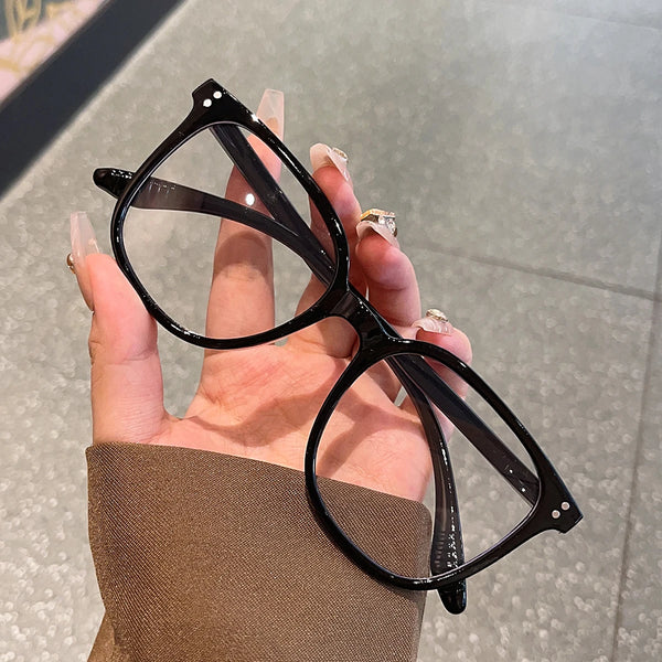 A hand holds a pair of black classic square frame sunglasses against a light gray background.