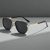 Gold-rimmed sunglasses with black lenses resting on a gray surface.