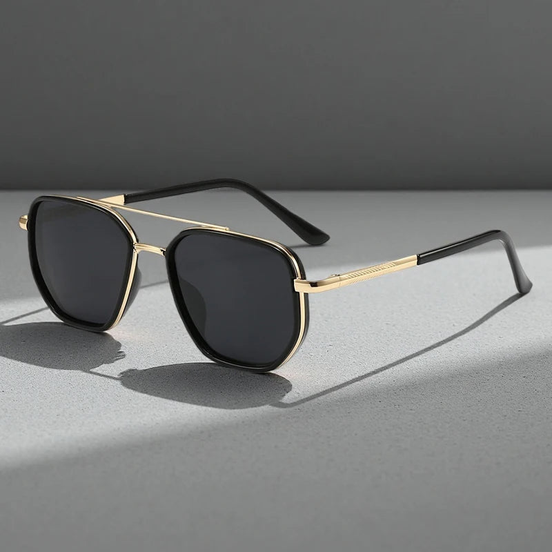Gold-rimmed sunglasses with black lenses resting on a gray surface.