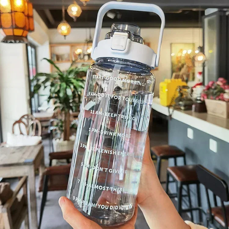 A hand holds a clear insulated water bottle with a white lid and straw, featuring motivational text on the body.
