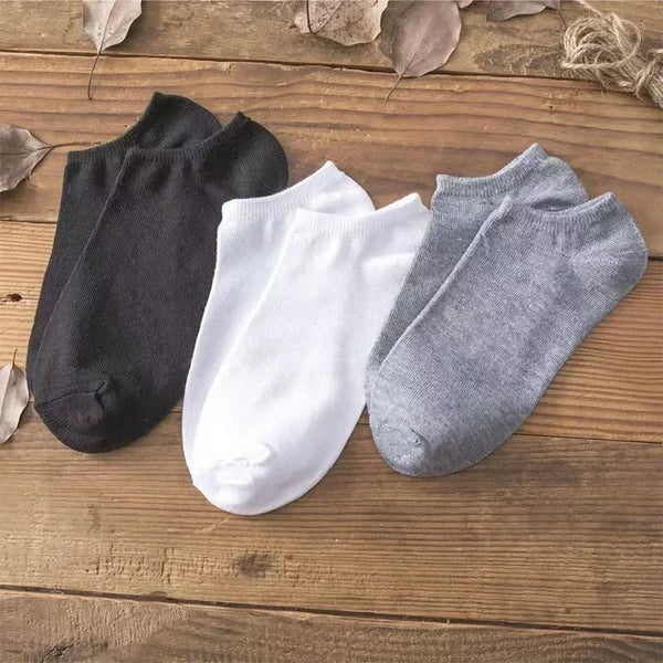 A set of three ankle socks in black, white, and gray laid on a wooden surface.