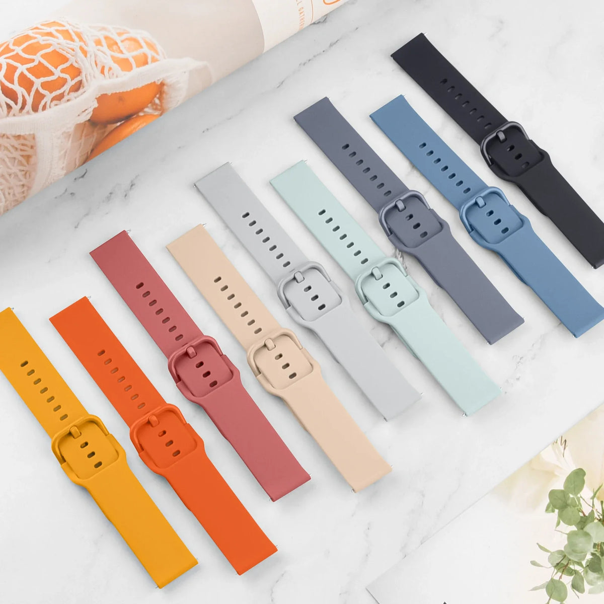A collection of silicone watch straps in various colors including orange, pink, beige, blue, and black laid out on a white ma