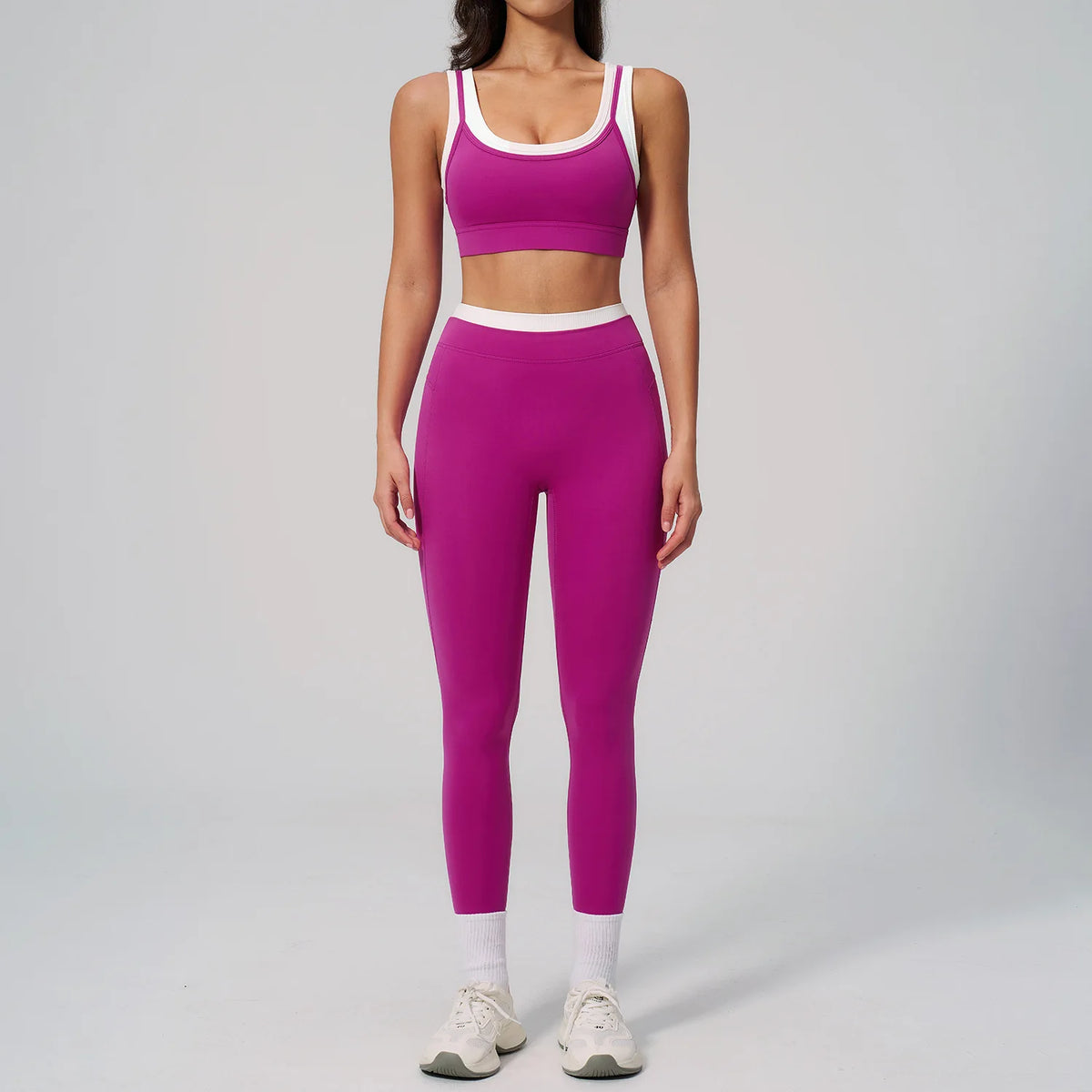 Eine Frau modelliert ein zweiteiliges Yoga- und Gym-Trainingsanzug in Magenta und Weiß.