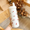 Une main tient un tumbler isotherme blanc avec une paille décorée de petites cerises rouges.