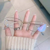 A hand holds a pair of clear, retro square frame eyeglasses against a light background.
