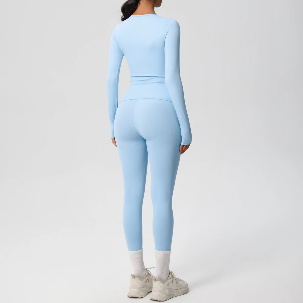 A woman wearing a light blue long-sleeved performance yoga set consisting of a long-sleeved top and leggings.