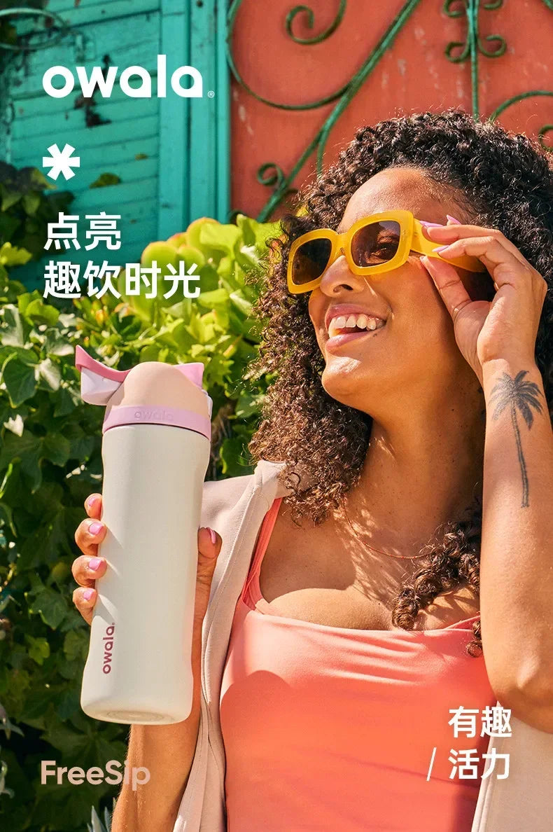 A woman holds an Owala insulated tumbler with a straw lid outdoors.