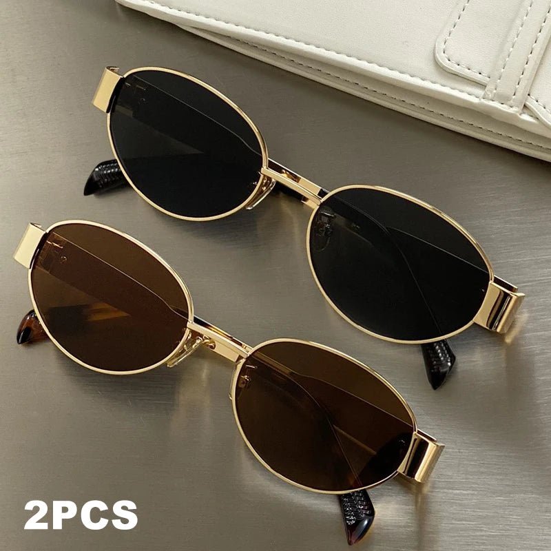A pair of classic oval metal sunglasses in gold and black are displayed on a neutral surface.