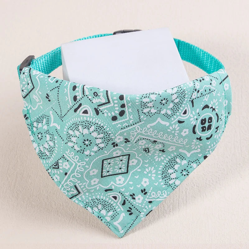A teal patterned fabric pet scarf with a white card tucked inside, shown against a light background.