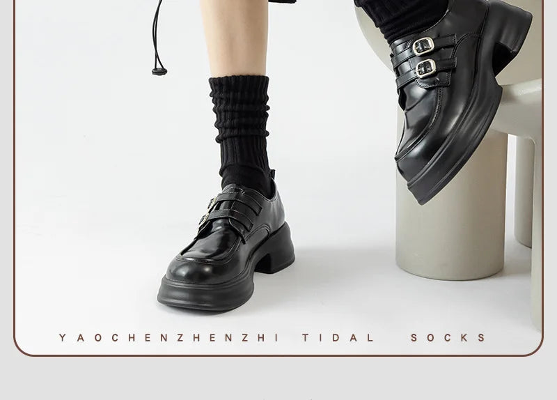 Black leather ankle boots paired with black socks shown in a studio shot.