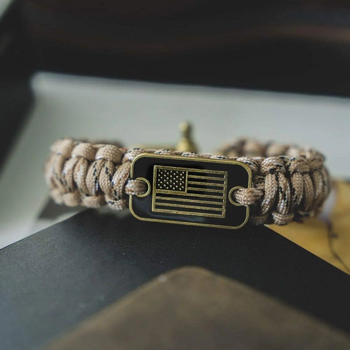 A tactical paracord survival bracelet with a black flag charm featuring the American flag design.