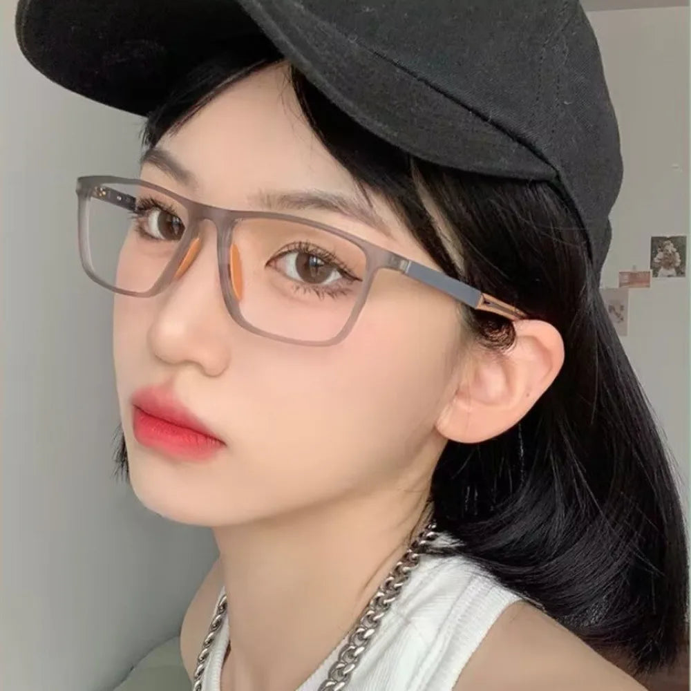 A close-up photo of a woman wearing rectangular, tortoise-shell framed sports reading glasses and a black fedora hat.