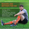 A man wearing orange calf compression sleeves is sitting on grass, demonstrating the product for use.