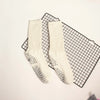 Pair of cream colored mid-calf yoga and pilates socks with a speckled pattern laid on a black grid mat.