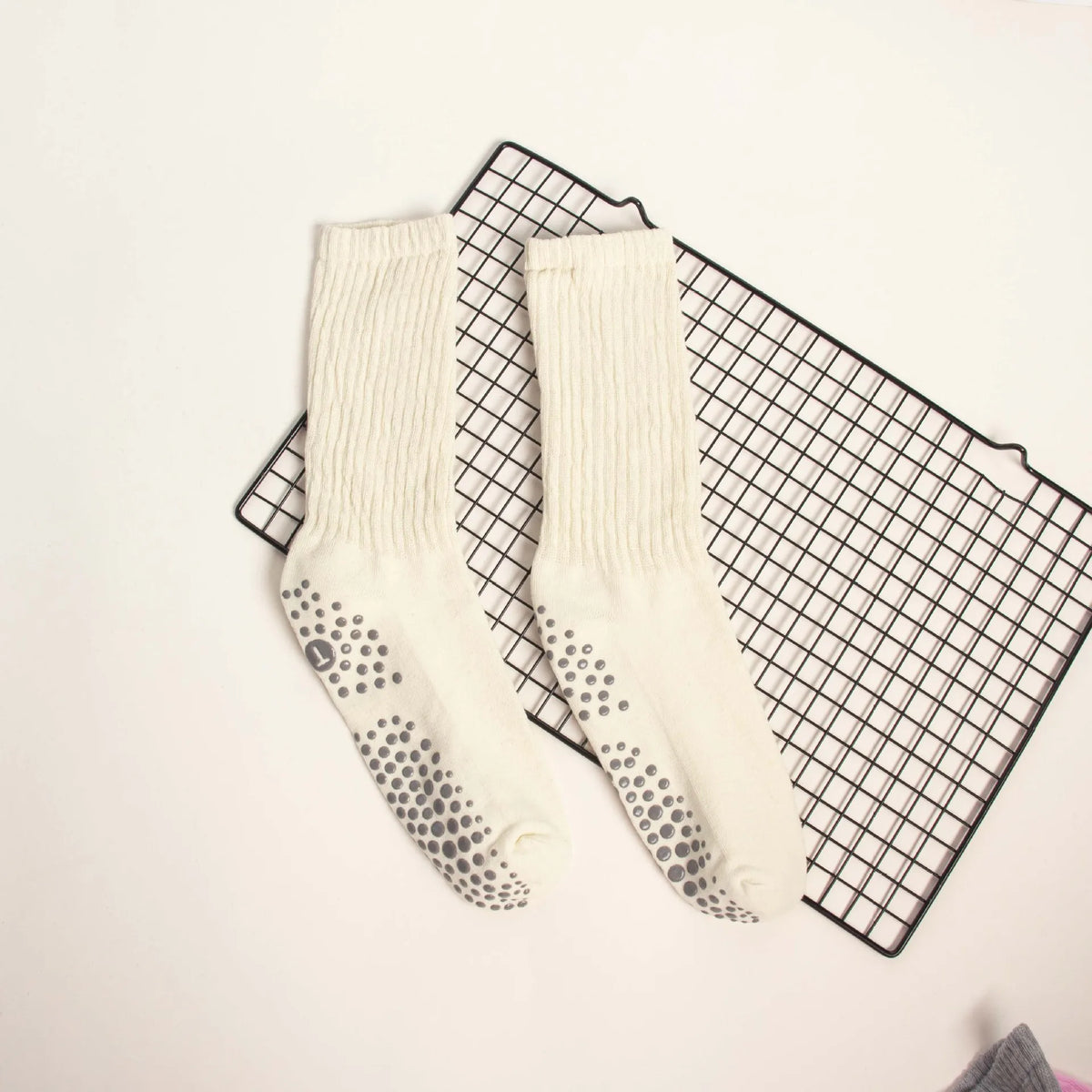 Pair of cream colored mid-calf yoga and pilates socks with a speckled pattern laid on a black grid mat.