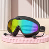 Un par de gafas de natación negras antiempañantes con lentes de colores brillantes sobre una superficie rosa.