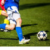 Un joueur de football en uniforme bleu et blanc frappe un ballon noir et blanc sur un terrain vert.