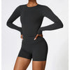 A woman models a long-sleeved, fitted black yoga and fitness t-shirt paired with matching black shorts.