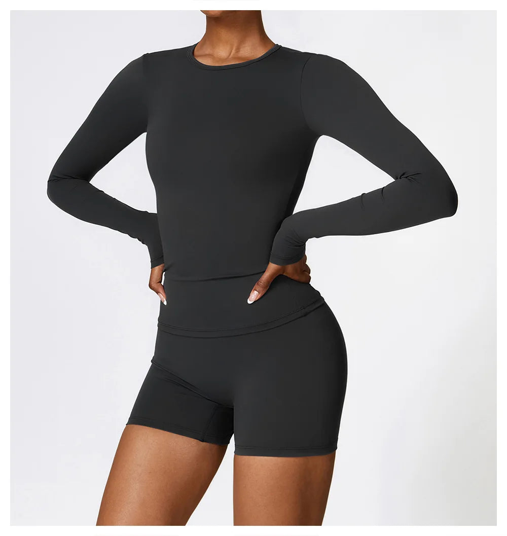 A woman models a long-sleeved, fitted black yoga and fitness t-shirt paired with matching black shorts.
