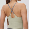 A woman wearing a light olive green athletic crisscross tank top and gray bottoms, shown from the back.