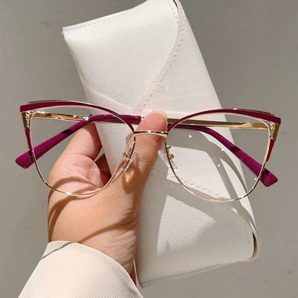 A hand holds a pair of purple-framed cat-eye blue light blocking glasses resting on a white leather case.