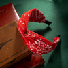Un accesorio para el cabello de tela roja y estampada junto a un libro encuadernado en cuero.