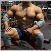 A muscular man wearing grey neoprene knee pads is sitting on a red weight bench.