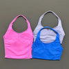 Three seamless performance yoga and gym tank tops in pink, gray, and blue laid side by side.
