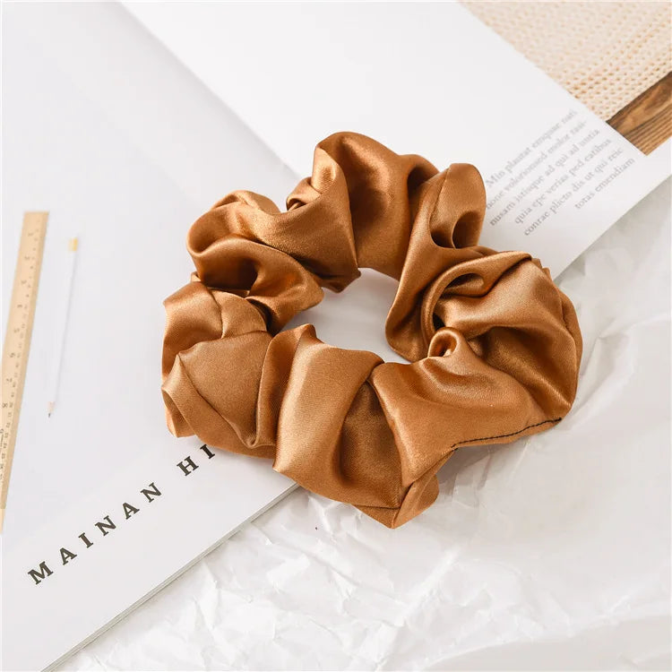 A brown satin scrunchie is shown on a white background next to a book.