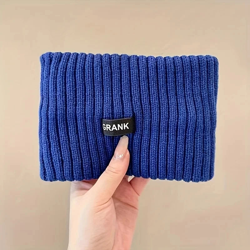 A hand is holding a dark blue knitted winter headwrap with a black tag.