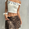 A woman wearing a white off-the-shoulder top and a leopard print casual skirt.