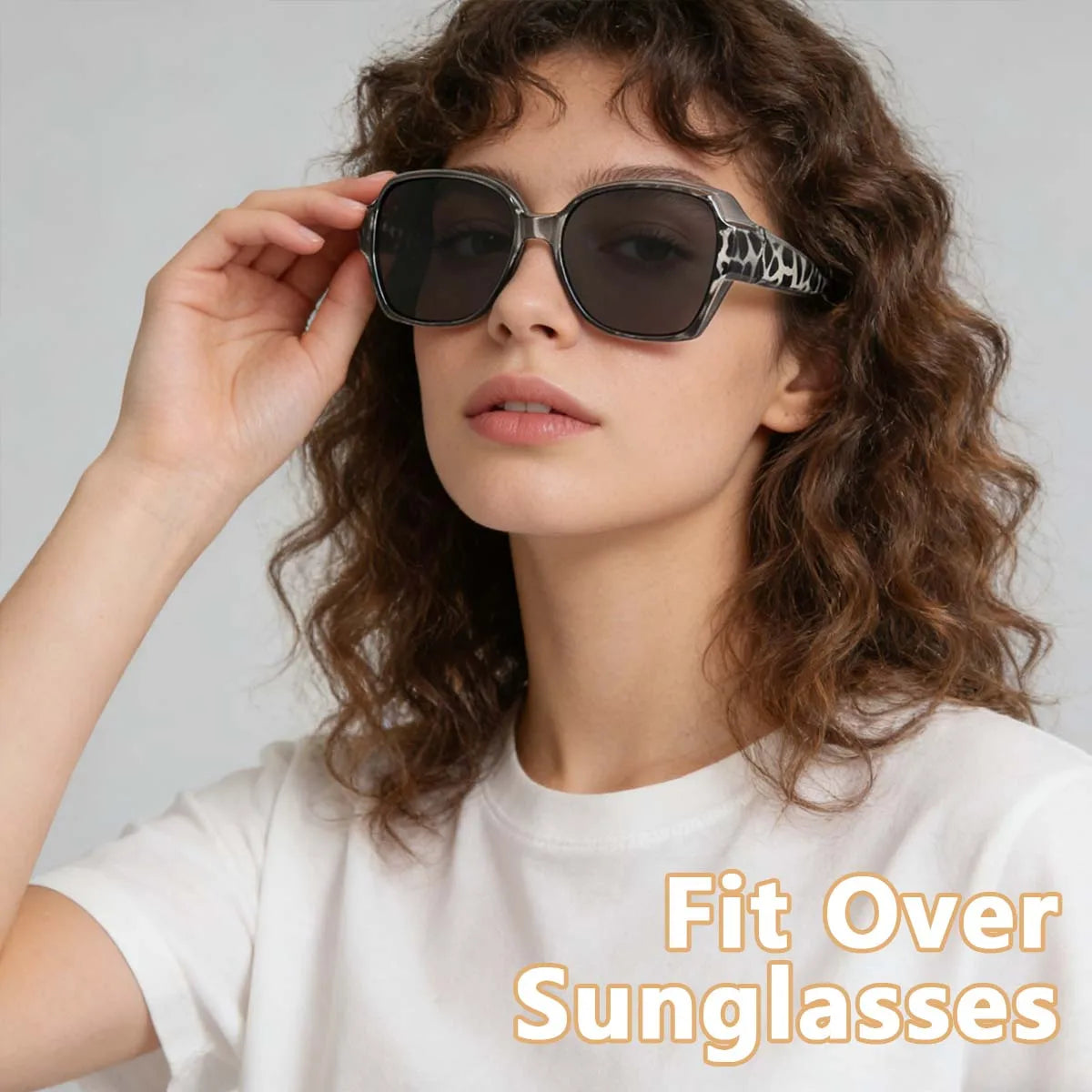 A woman models wrap-around sunglasses with glasses compatibility against a light gray background.