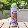 A purple cartoon drinking water bottle with a bear design and a clear straw, sitting on a wooden surface.