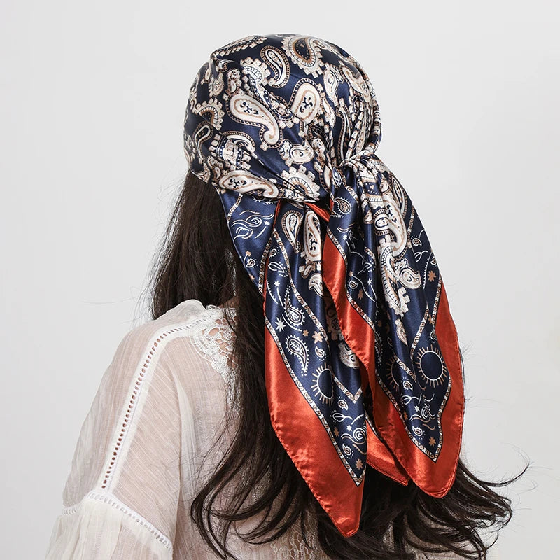 A woman is wearing a blue and white paisley silk shawl scarf tied around her hair, visible over a light-colored garment.
