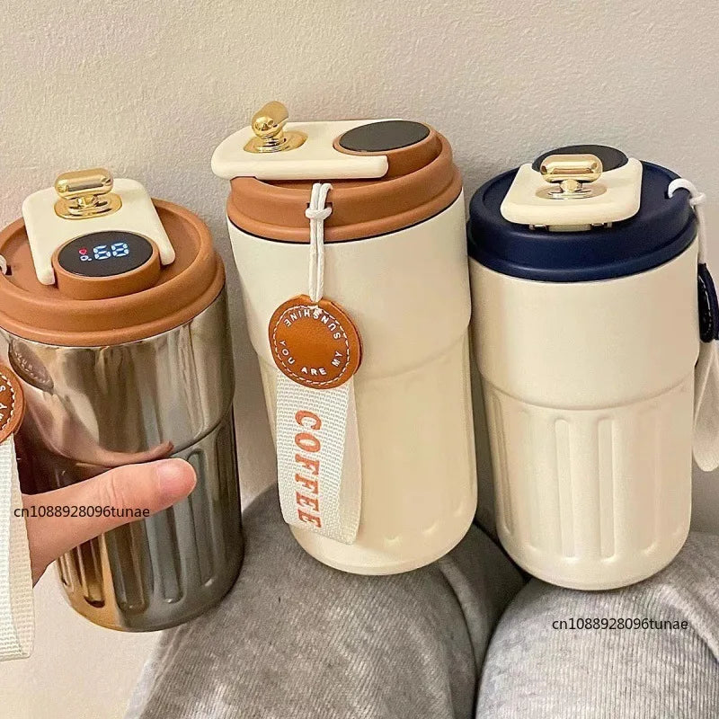 A set of ceramic thermo mugs with gold accents and LED temperature displays sitting on a gray fabric.