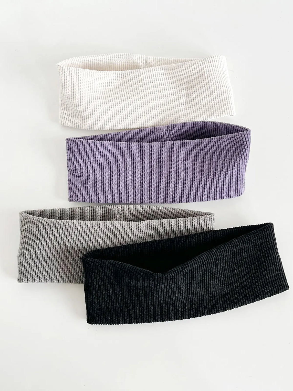 Un paquete de cuatro bandas elásticas para el cabello en blanco, morado, gris y negro.
