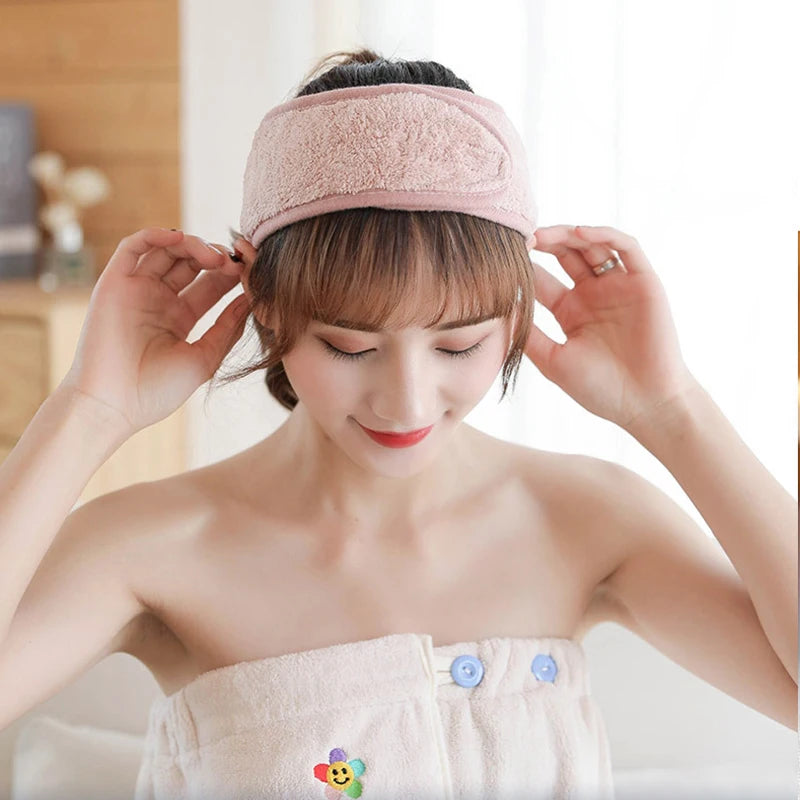A woman is wearing a pink faux fur headband and a matching top, with her hands adjusting the hair.