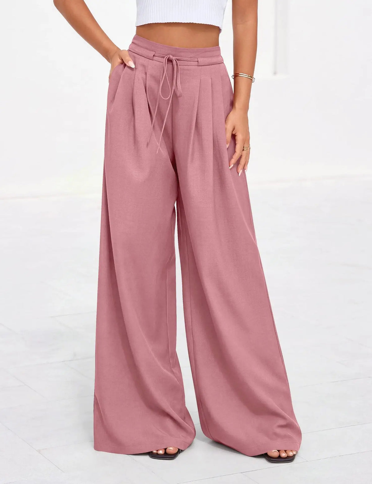 A model wearing dusty rose flowy high waist drawstring wide leg pants and a white cropped top.