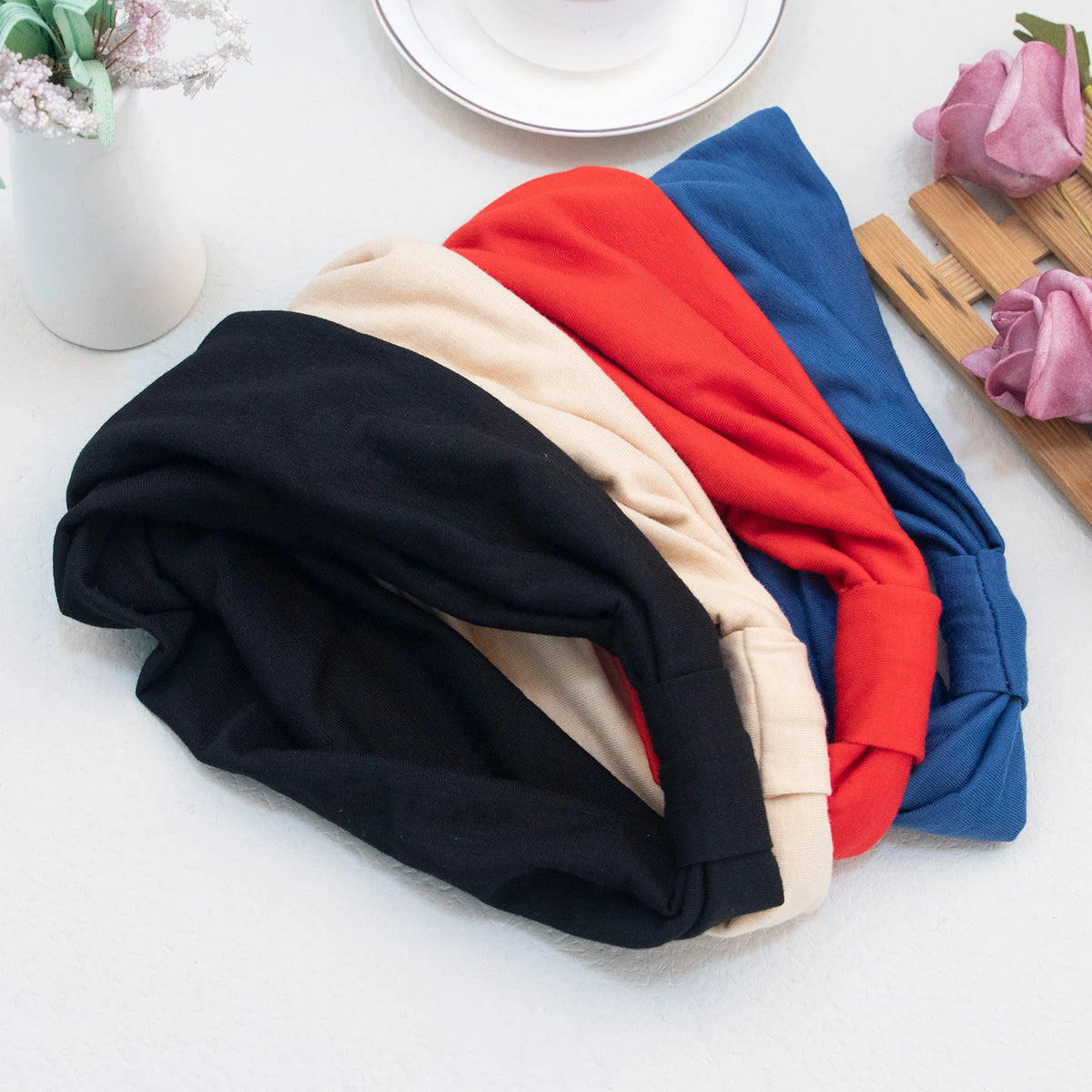 Eine Sammlung von fünf weichen elastischen breiten Stirnbändern in Schwarz, Beige, Rot, Blau und Marineblau, gestapelt auf ei