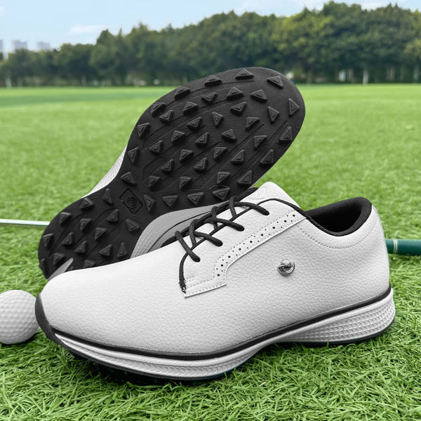A pair of white and gray lightweight men's golf training shoes with black traction soles resting on green grass.