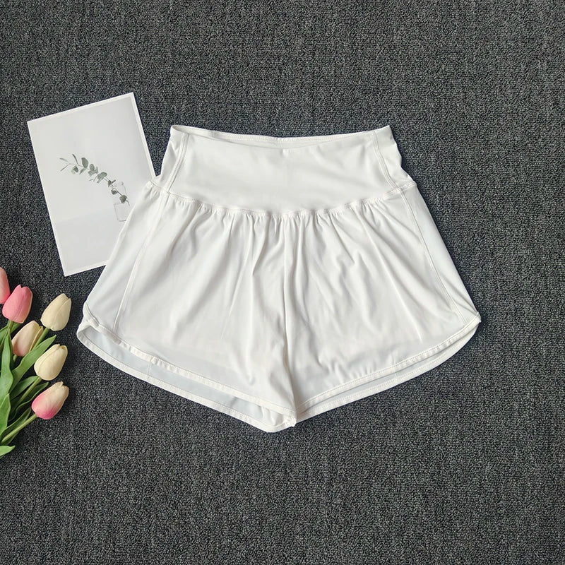 White women's high-waist yoga and fitness shorts laid flat on a dark gray surface with a white card nearby.