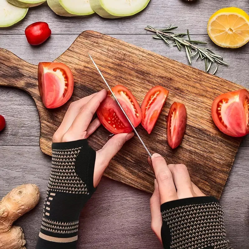Hands wearing black knit wrist compression braces preparing fresh tomatoes on a wooden cutting board.