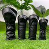 A pair of black premium wooden golf club head covers resting on green grass.